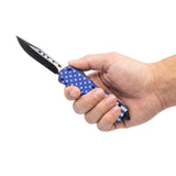 7‑inch automatic OTF knife with American flag handle shown in hand to display size, grip, and drop‑point blade.