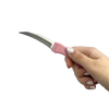 Curved pink comb‑style knife held in hand, showing the concealed blade integrated into the comb design.