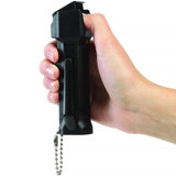  Close view of a person gripping the Mace 3‑in‑1 Police pepper spray, showing thumb placement for lifting the flip‑top safety cover.
