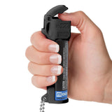 Close view of a person gripping the Mace 3‑in‑1 Police pepper spray, showing thumb placement for lifting the flip‑top safety cover.